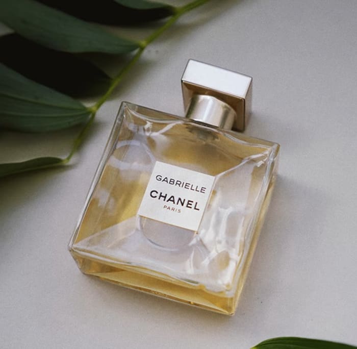 Gabrielle Essence Eau De Parfum bottle on a table with green leaves